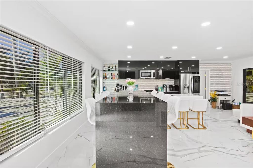 A modern kitchen features a black granite island, white marble floors, and glossy black cabinetry — 6612 9TH AVENUE NW, BRADENTON, FL