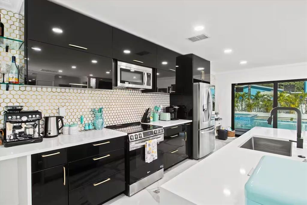 A modern kitchen features black high-gloss cabinets, white countertops, and a gold honeycomb backsplash — 6612 9TH AVENUE NW, BRADENTON, FL