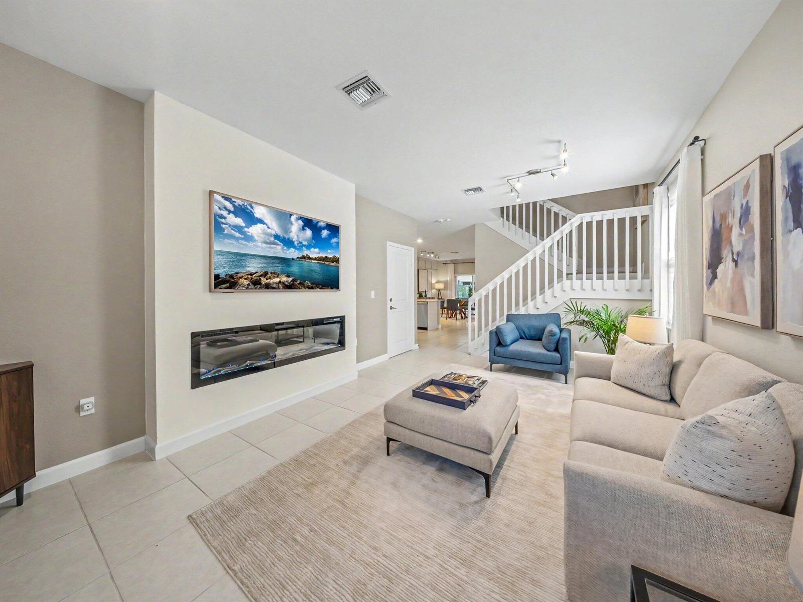 A living room features a wall-mounted television above a linear fireplace and a staircase — 11968 NW 47th Manor, Coral Springs FL 33076, CORAL SPRINGS, FL