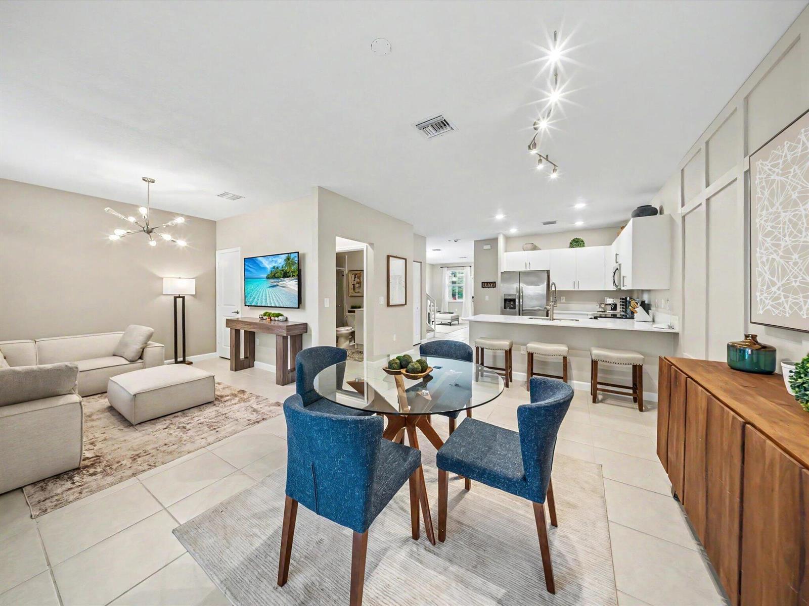 An open-concept living and dining area features a modern kitchen, tile floors, and blue chairs — 11968 NW 47th Manor, Coral Springs FL 33076, CORAL SPRINGS, FL