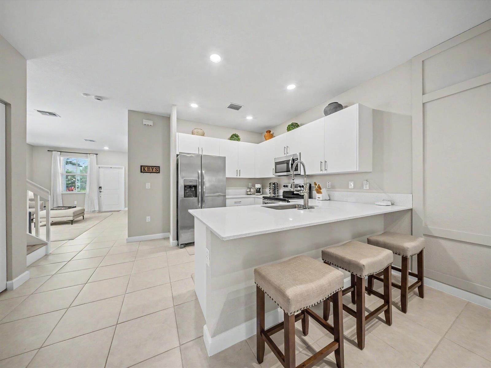 A kitchen features white cabinets, stainless steel appliances, a quartz countertop, and three bar stools — 11968 NW 47th Manor, Coral Springs FL 33076, CORAL SPRINGS, FL