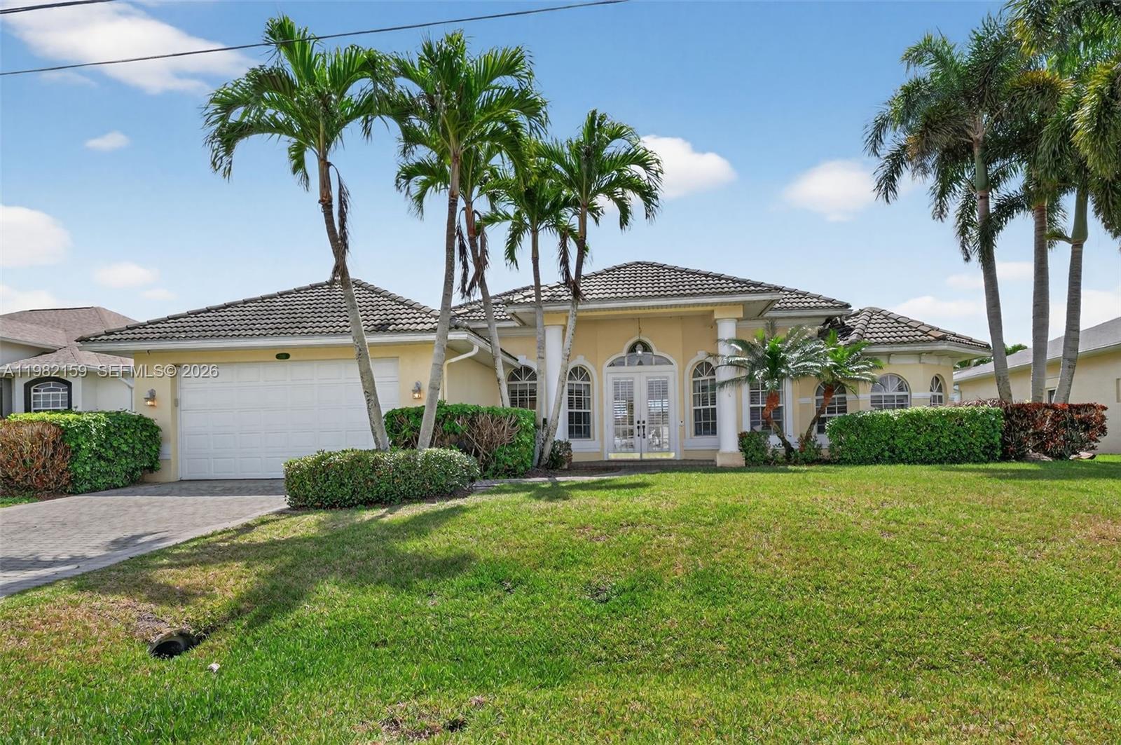 A single-story yellow house with a tile roof, white columns, and palm trees in front — 1414 NE 2nd Ter, Cape Coral FL 33909, CAPE CORAL, FL