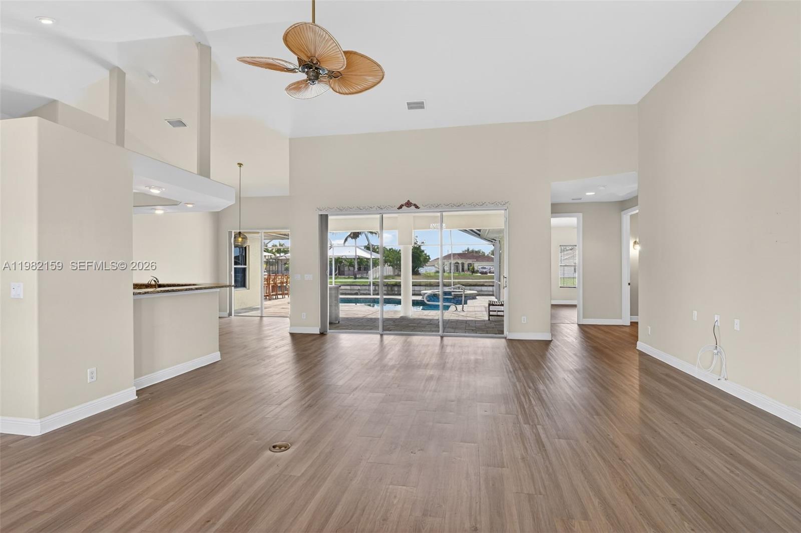 This open-concept living area features wood-look flooring, a ceiling fan, and sliding glass patio doors — 1414 NE 2nd Ter, Cape Coral FL 33909, CAPE CORAL, FL
