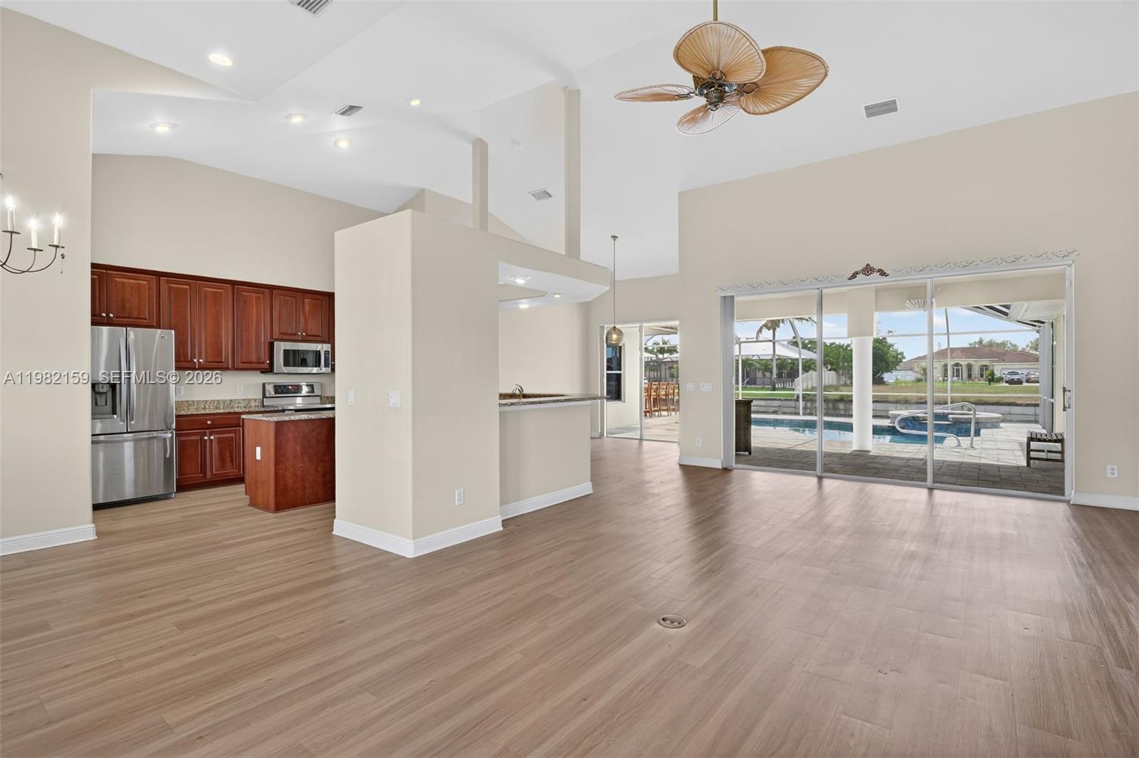 An open-concept kitchen and living area with wood-look flooring and sliding doors to a pool — 1414 NE 2nd Ter, Cape Coral FL 33909, CAPE CORAL, FL