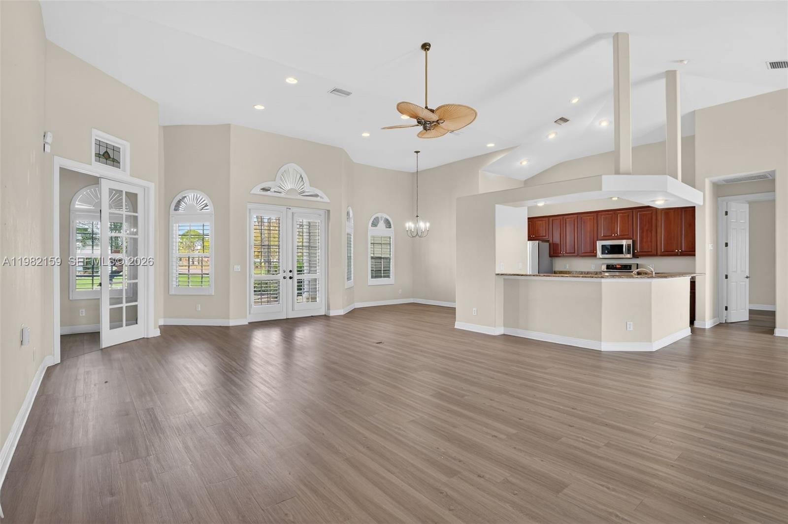 An open-concept living area features wood-look flooring, a vaulted ceiling, and an attached kitchen — 1414 NE 2nd Ter, Cape Coral FL 33909, CAPE CORAL, FL