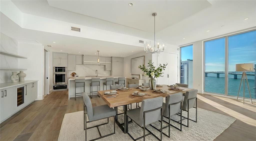 A modern dining area and kitchen feature light wood floors, gray cabinetry, and waterfront views — 253 GOLDEN GATE POINT UNIT 902, SARASOTA, FL