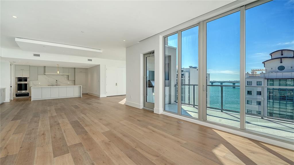 An open-concept living area with light wood floors, a modern kitchen, and floor-to-ceiling windows — 253 GOLDEN GATE POINT UNIT 902, SARASOTA, FL