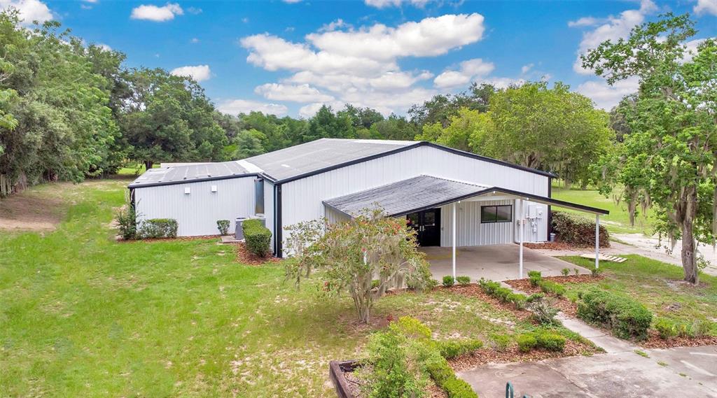 A white metal-sided building with a covered entrance sits on a grassy, tree-lined lot — 31336 COUNTY ROAD 437, SORRENTO, FL