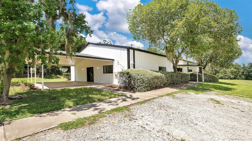 A white metal building with a covered carport stands on a grassy lot with trees — 31336 COUNTY ROAD 437, SORRENTO, FL