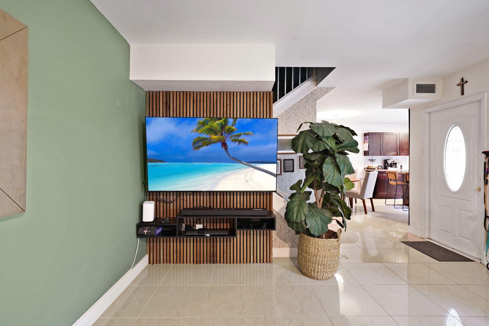 A living room features a wall-mounted television on wood slats, a floating shelf, and a plant — 8910 SW 20th Place # 23, Davie FL 33324, DAVIE, FL
