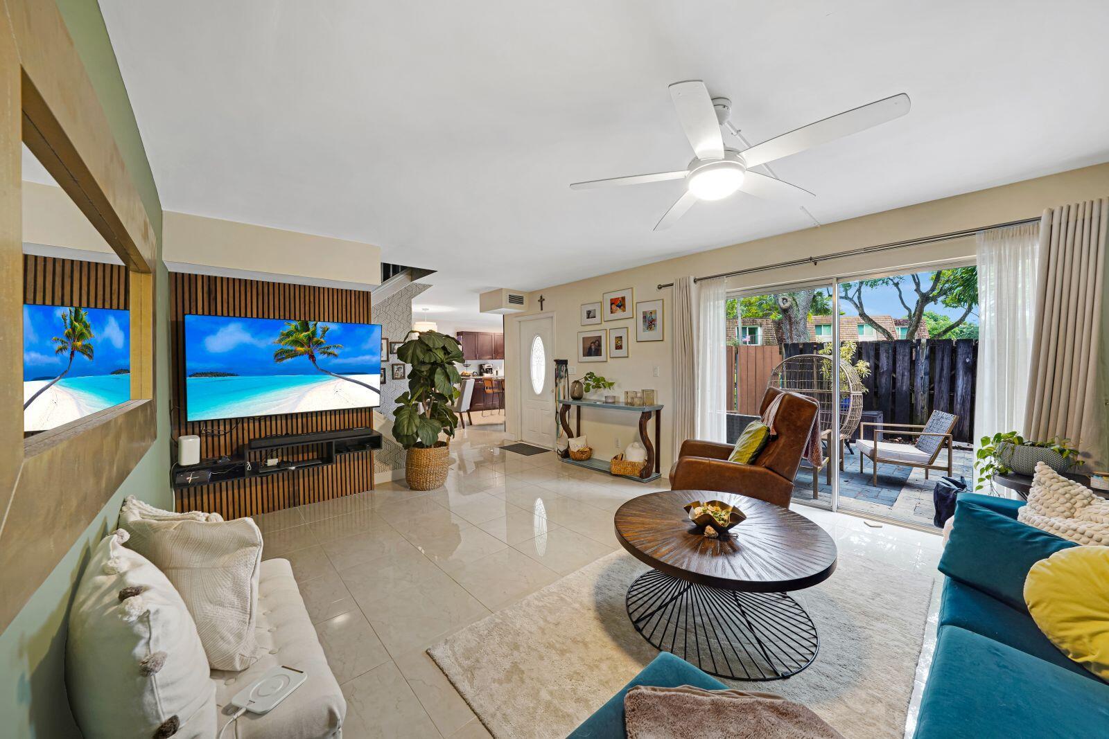 A living room with tile floors, a wall-mounted television, and a sliding door to a patio — 8910 SW 20th Place # 23, Davie FL 33324, DAVIE, FL