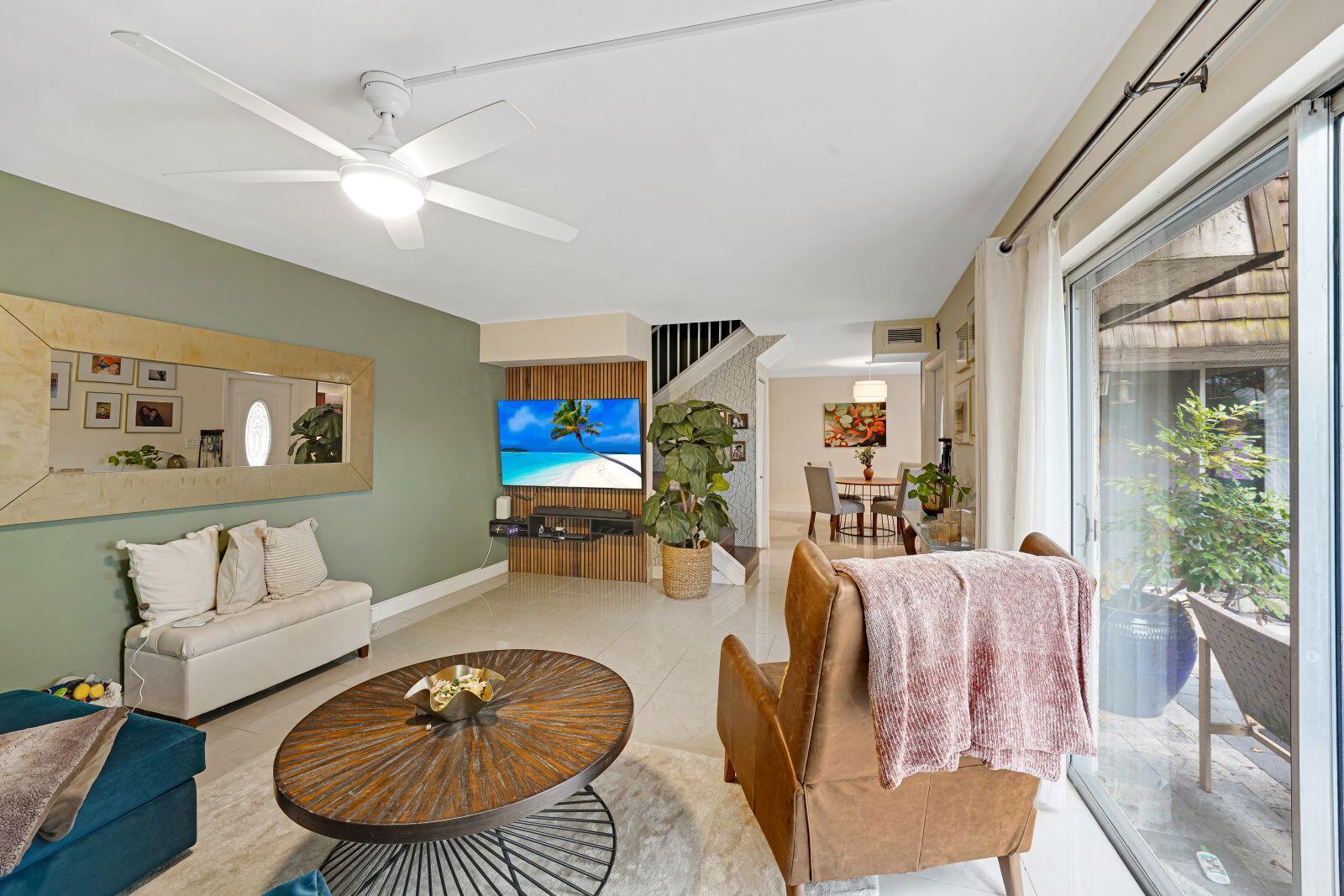 A living room with a green accent wall, wood-slat TV feature, and sliding glass doors — 8910 SW 20th Place # 23, Davie FL 33324, DAVIE, FL