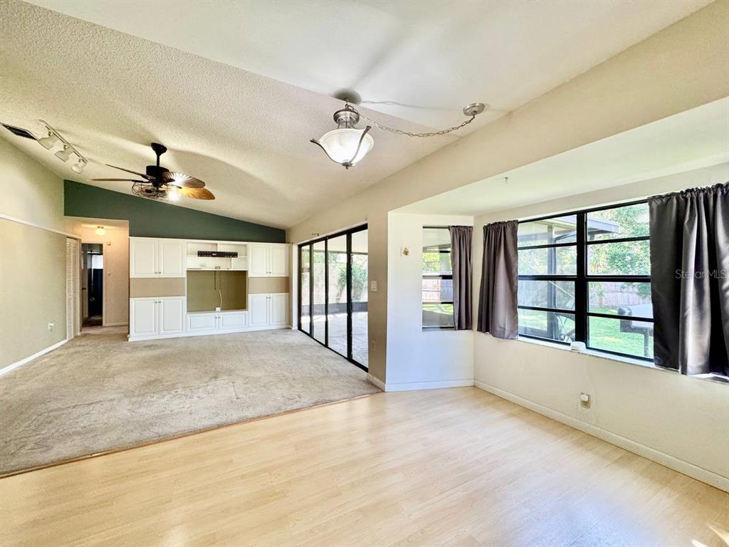 A living room features light wood flooring, carpeted area, built-in cabinetry, and large windows — 3195 CHAMBLEE LANE, CLEARWATER, FL