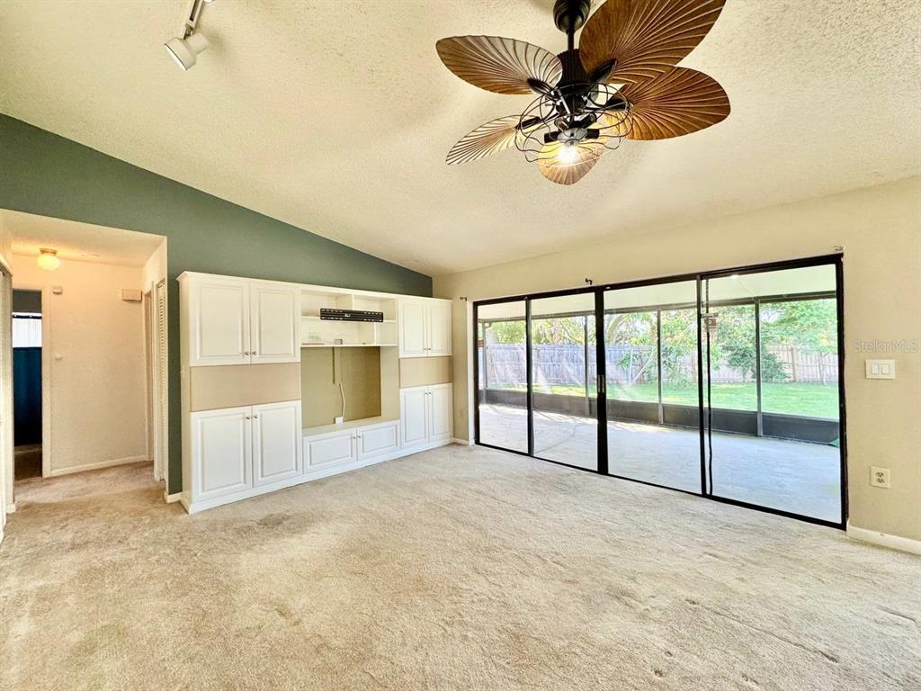 A living room features beige carpeting, a built-in white entertainment center, and sliding glass doors — 3195 CHAMBLEE LANE, CLEARWATER, FL