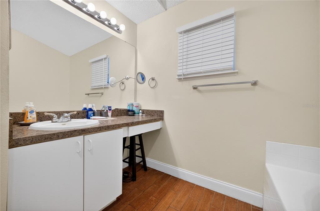 A bathroom features a white vanity with a brown countertop, a large mirror, and wood-look flooring — 953 GASCONY COURT, KISSIMMEE, FL