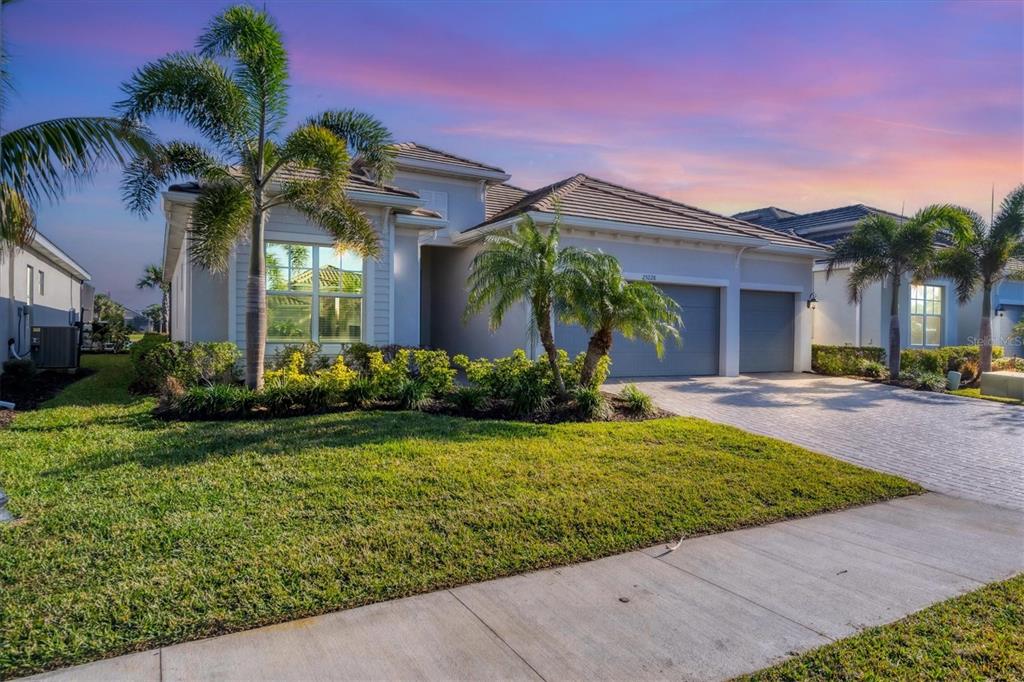 A single-story house with a paved driveway, two-car garage, and palm trees at sunset — 25228 LONGMEADOW DRIVE, PUNTA GORDA, FL
