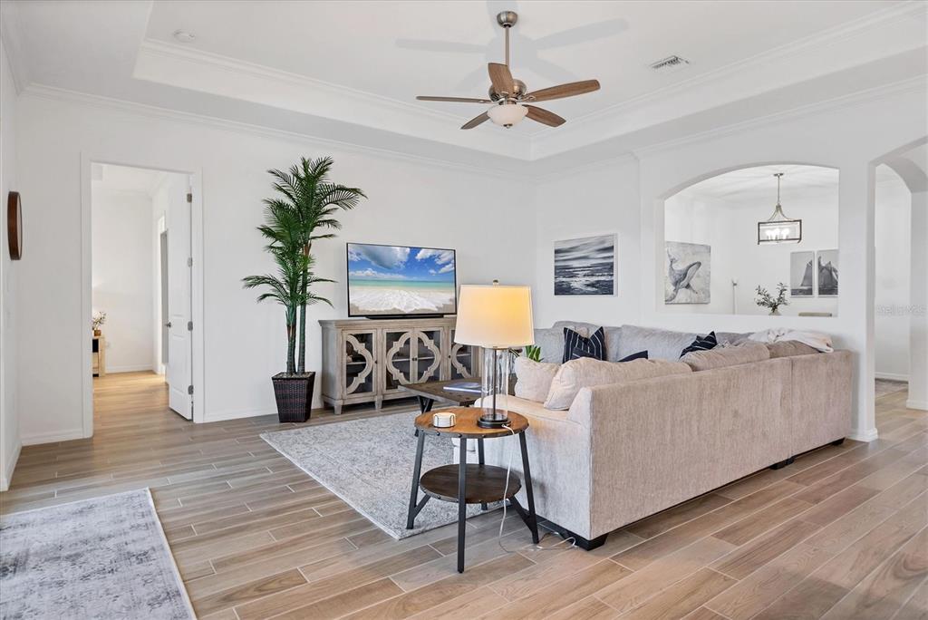 A living room features a tray ceiling, light wood-look tile flooring, and a sectional sofa — 25228 LONGMEADOW DRIVE, PUNTA GORDA, FL