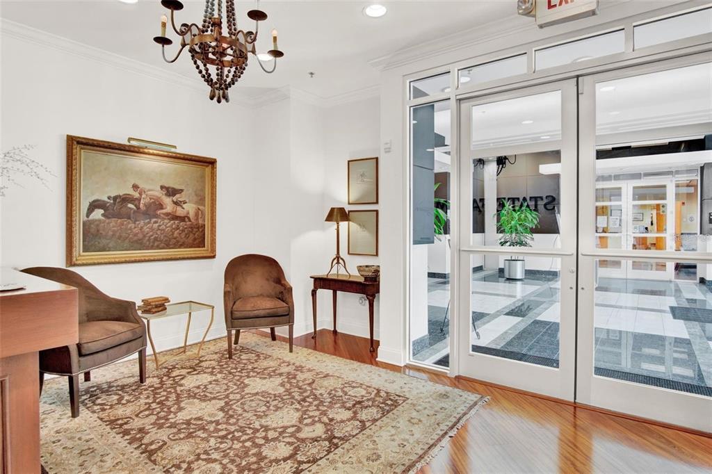A lobby features two brown armchairs, a patterned rug, a chandelier, and glass entry doors — 6200 METROWEST BOULEVARD UNIT 103D, ORLANDO, FL