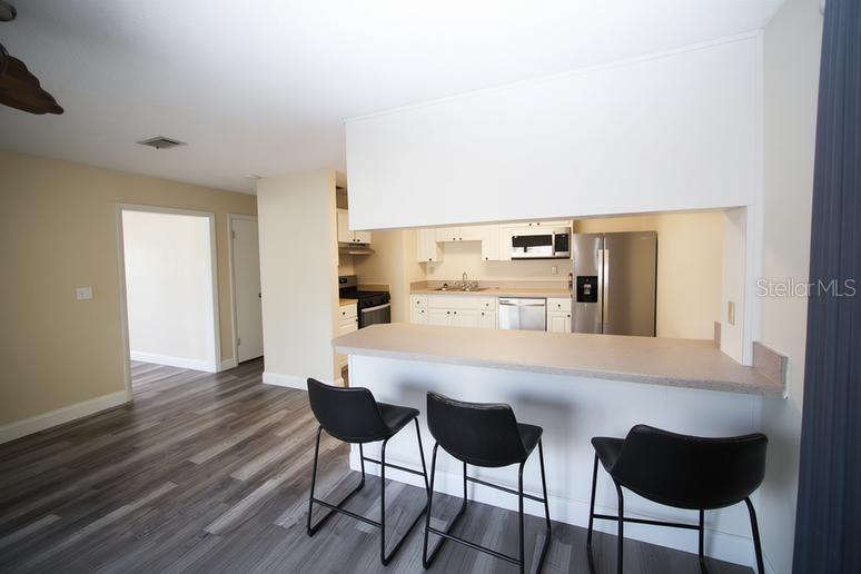 A kitchen with white cabinets and stainless steel appliances overlooks a breakfast bar with stools — 141 W CONNECTICUT AVENUE, EDGEWATER, FL