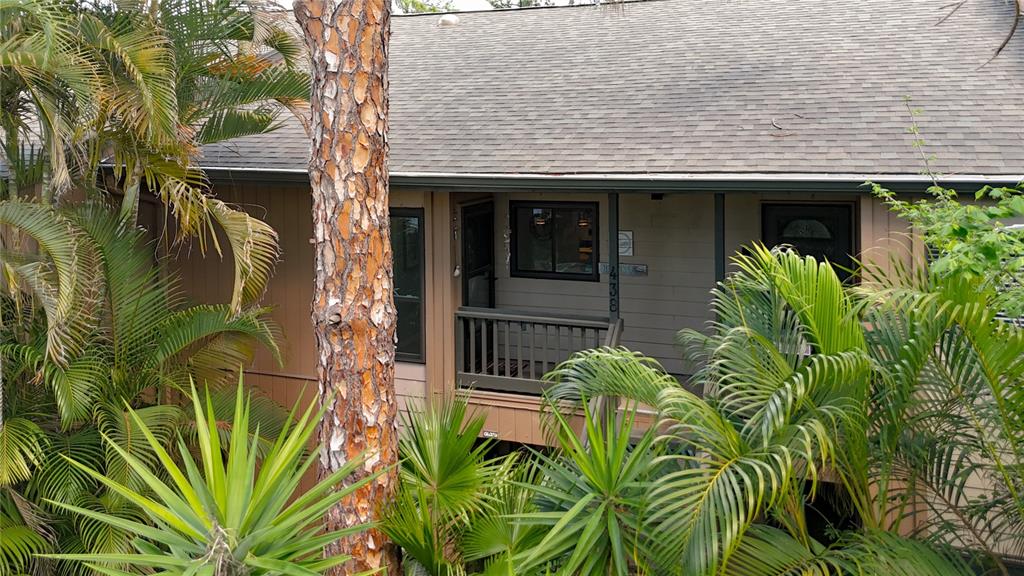 A view of a tan house exterior with a wooden porch, surrounded by palm trees — 1715 PELICAN COVE ROAD UNIT GL438, SARASOTA, FL