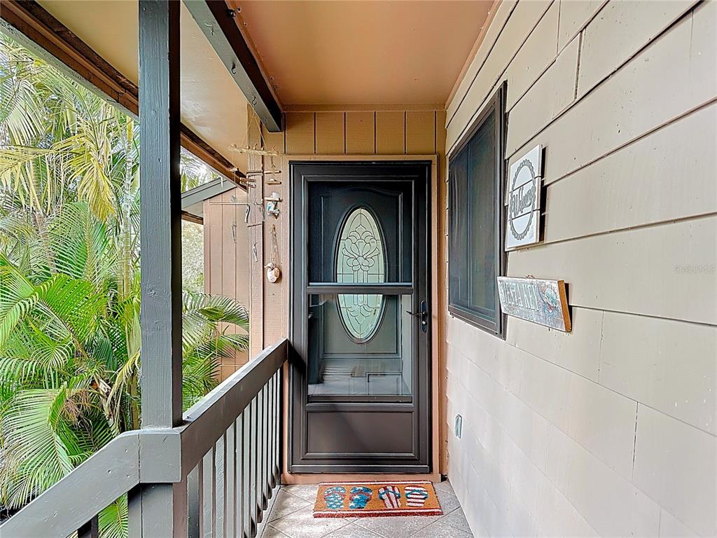 A covered exterior entryway features a dark storm door, beige siding, and a palm tree — 1715 PELICAN COVE ROAD UNIT GL438, SARASOTA, FL