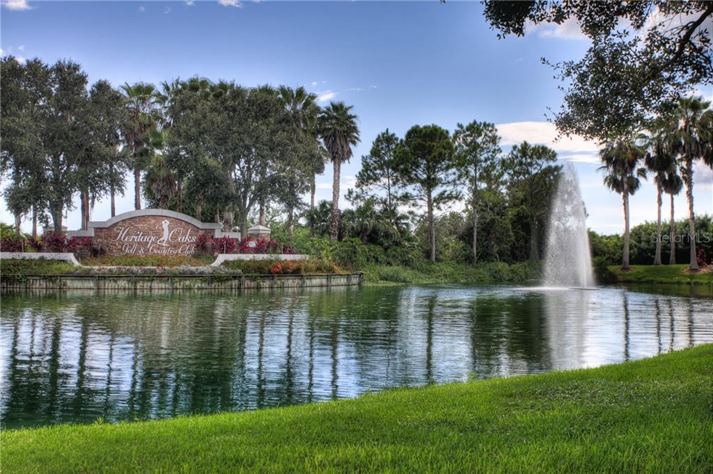 A fountain sprays water in a pond in front of a Heritage Oaks entrance sign — 5270 HYLAND HILLS AVENUE UNIT 1722, SARASOTA, FL