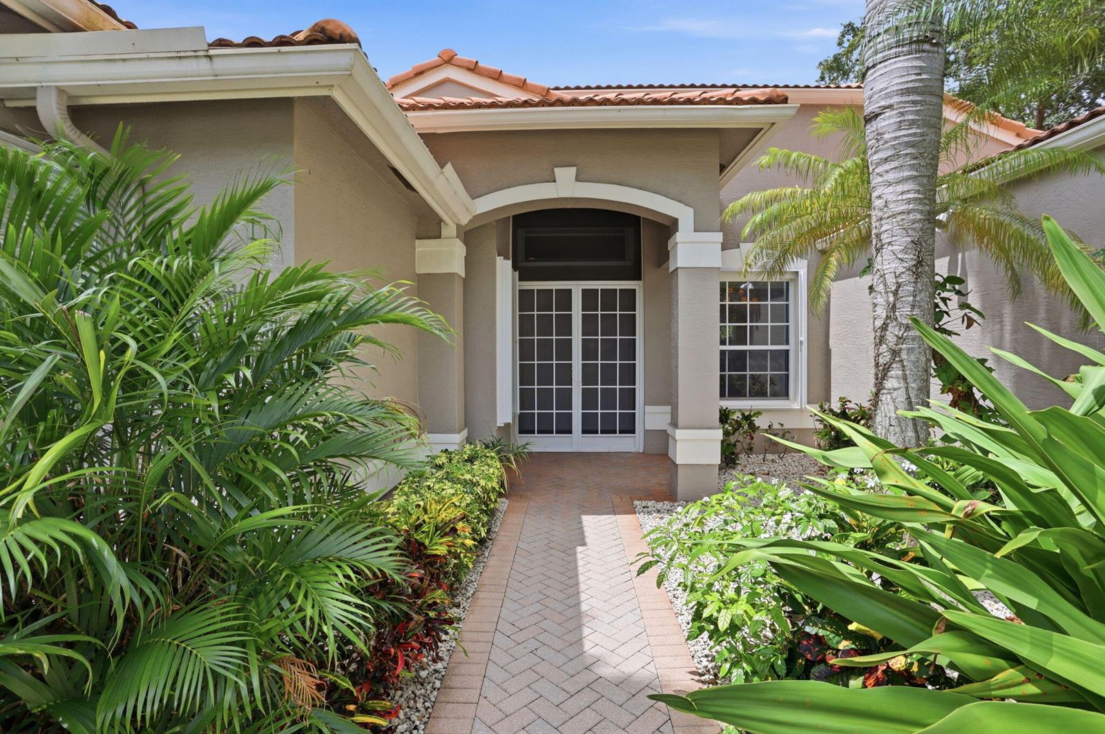 A brick walkway leads to the double front doors of a tan stucco house — 7527 Monticello Way, Boynton Beach FL 33437, BOYNTON BEACH, FL