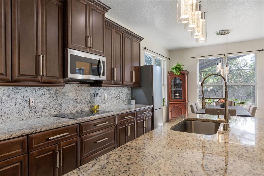 A kitchen with dark wood cabinets, granite countertops, a stainless steel sink, and pendant lighting — 38 BREWSTER LANE, PALM COAST, FL