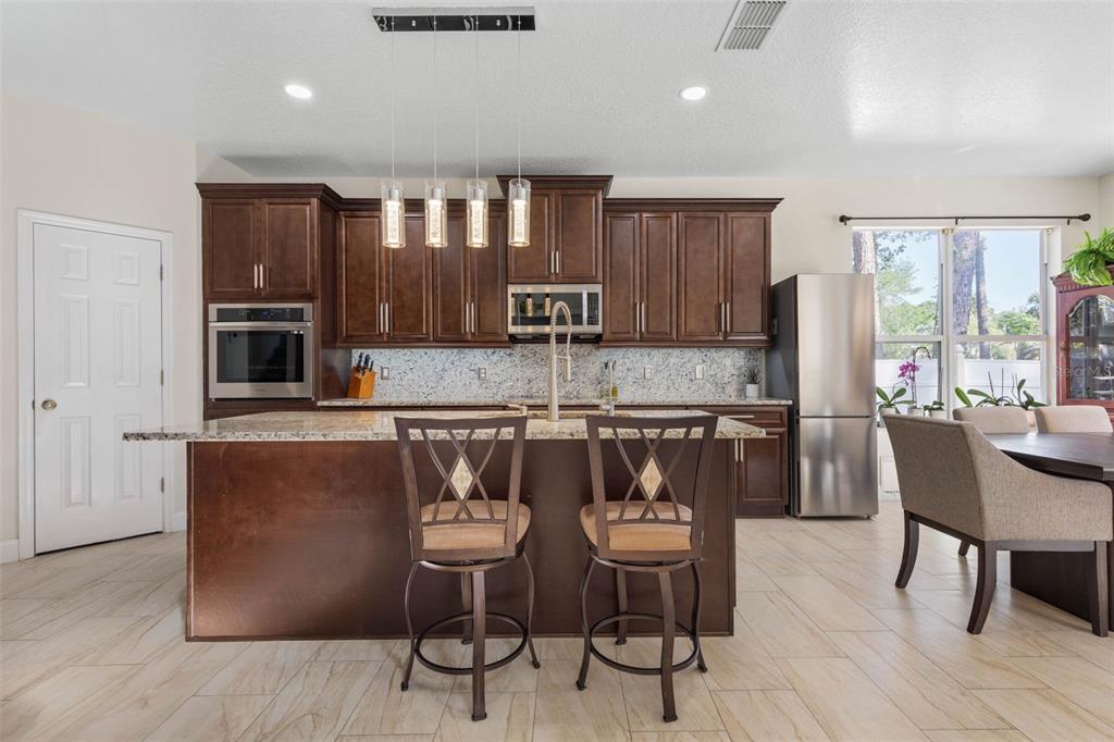 A kitchen with dark wood cabinets, granite countertops, a center island, and stainless steel appliances — 38 BREWSTER LANE, PALM COAST, FL