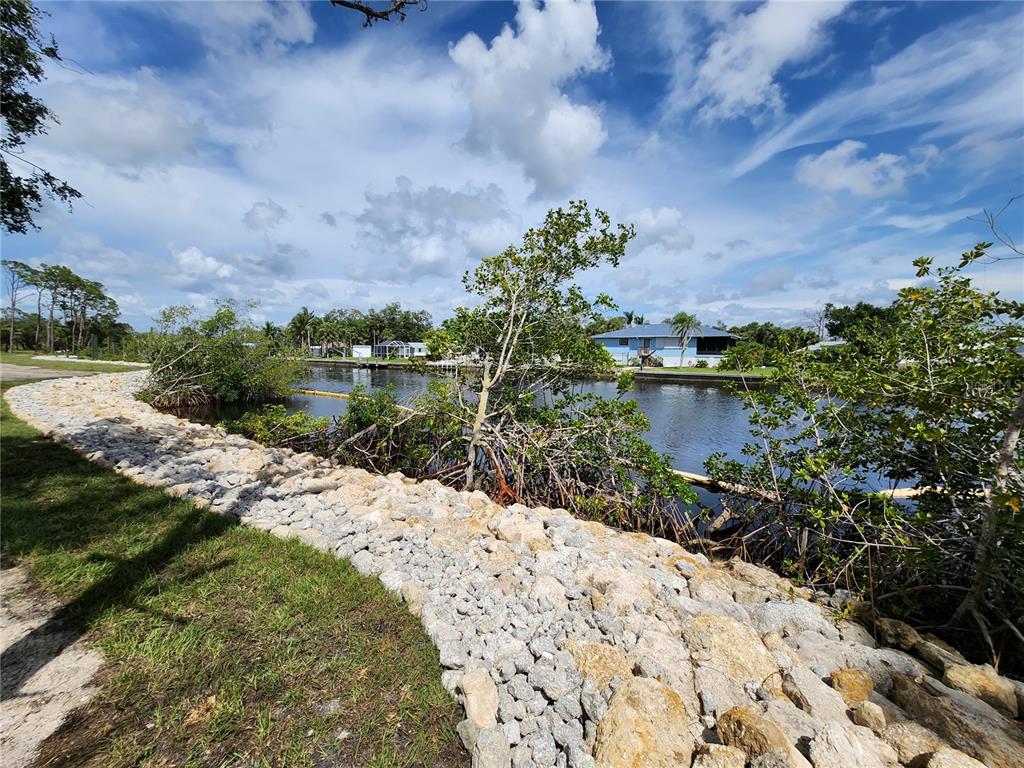 A rocky shoreline borders a canal with mangroves and a house in the background — 971 LAMPP DRIVE, ENGLEWOOD, FL