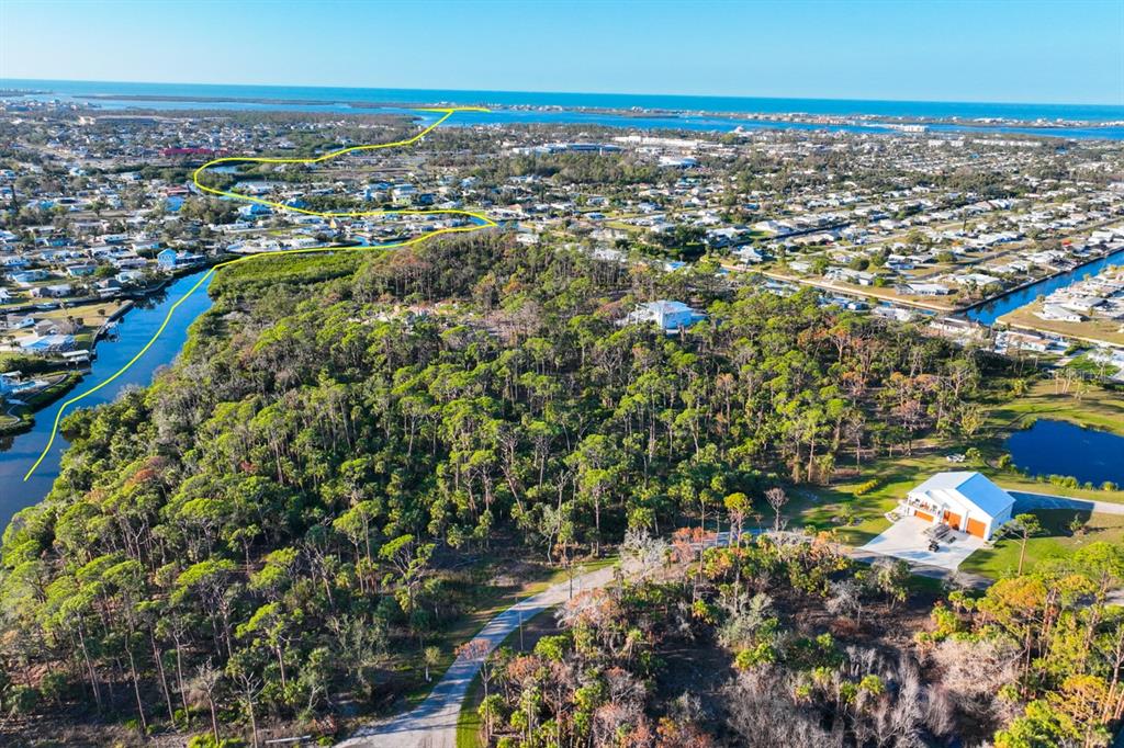 An aerial view shows a wooded lot, a large white building, and a winding waterway — 971 LAMPP DRIVE, ENGLEWOOD, FL