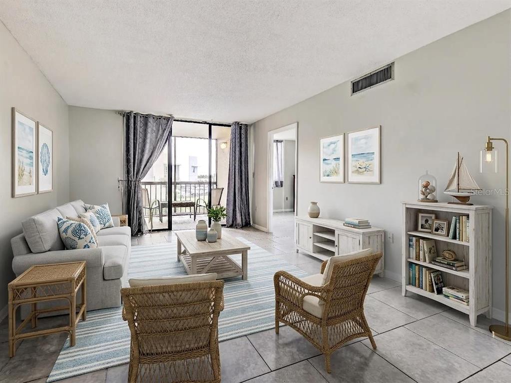A living room with tile floors, a sofa, two wicker chairs, and a balcony view — 3006 CARING WAY UNIT 210, PORT CHARLOTTE, FL