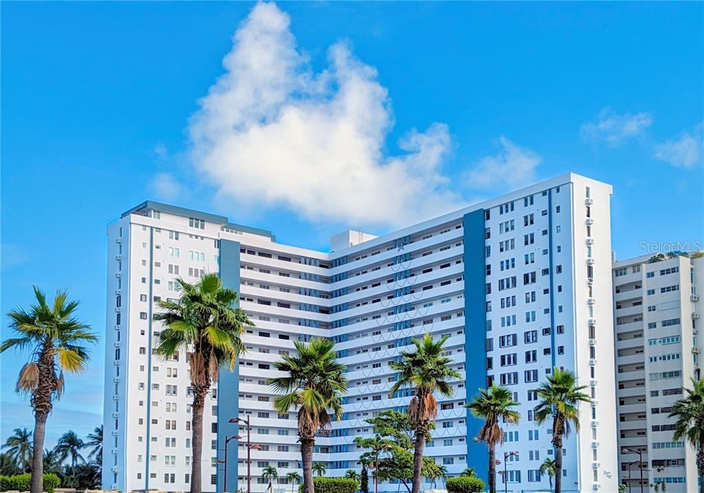 A tall, white multi-story apartment building stands under a bright blue sky with palm trees — 4327 ISLA VERDE AVENUE UNIT PH 1506, CAROLINA, PR