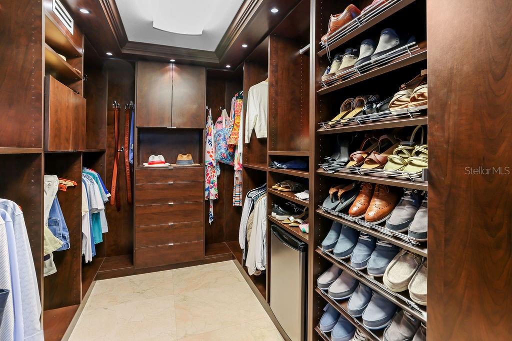 A walk-in closet features dark wood cabinetry, built-in shelving for shoes, and hanging garment rods — 4327 ISLA VERDE AVENUE UNIT PH 1506, CAROLINA, PR