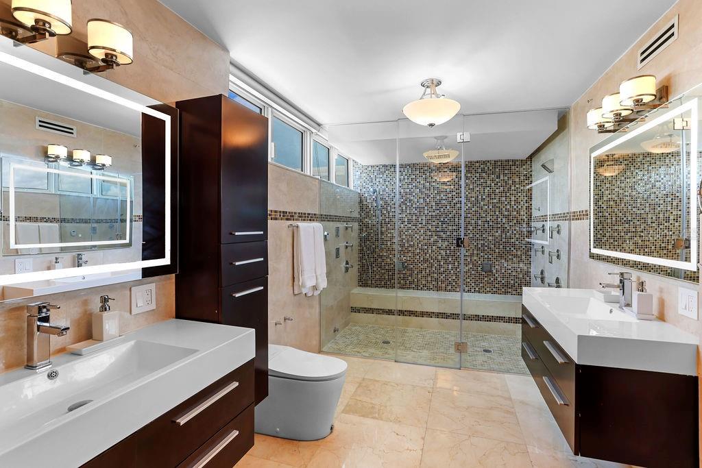 A modern bathroom features dual vanities, a glass-enclosed walk-in shower, and beige stone tile flooring — 4327 ISLA VERDE AVENUE UNIT PH 1506, CAROLINA, PR