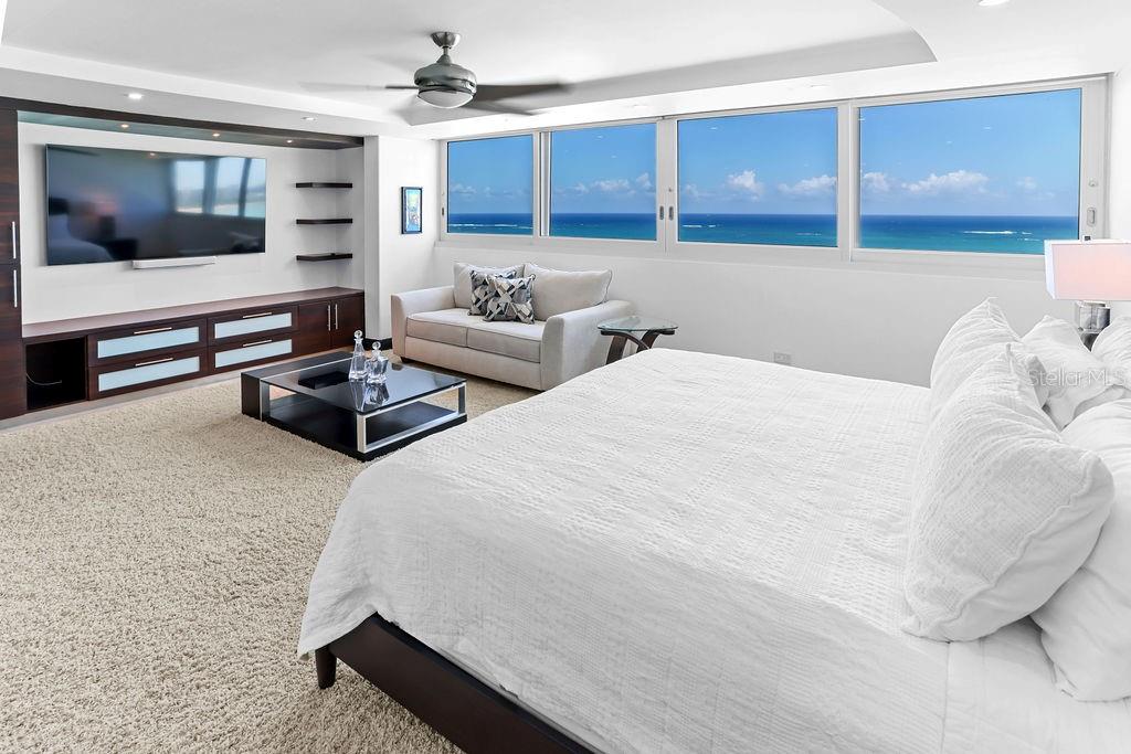 A bedroom features a large bed, a seating area, and floor-to-ceiling windows overlooking the ocean — 4327 ISLA VERDE AVENUE UNIT PH 1506, CAROLINA, PR