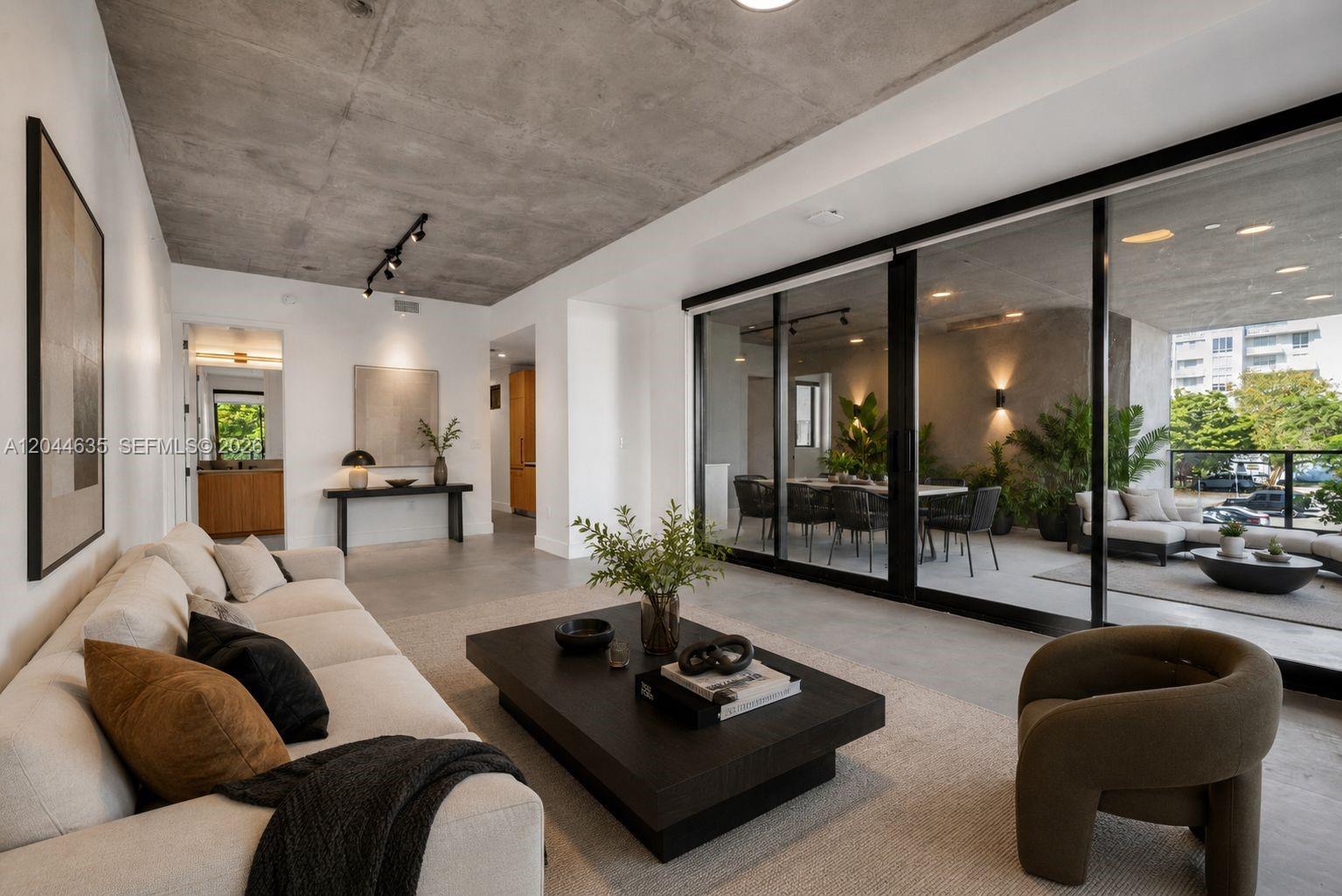 A modern living room features a concrete ceiling, white walls, and large sliding glass doors — 91 NW 27th St # 101, Miami FL 33127, MIAMI, FL