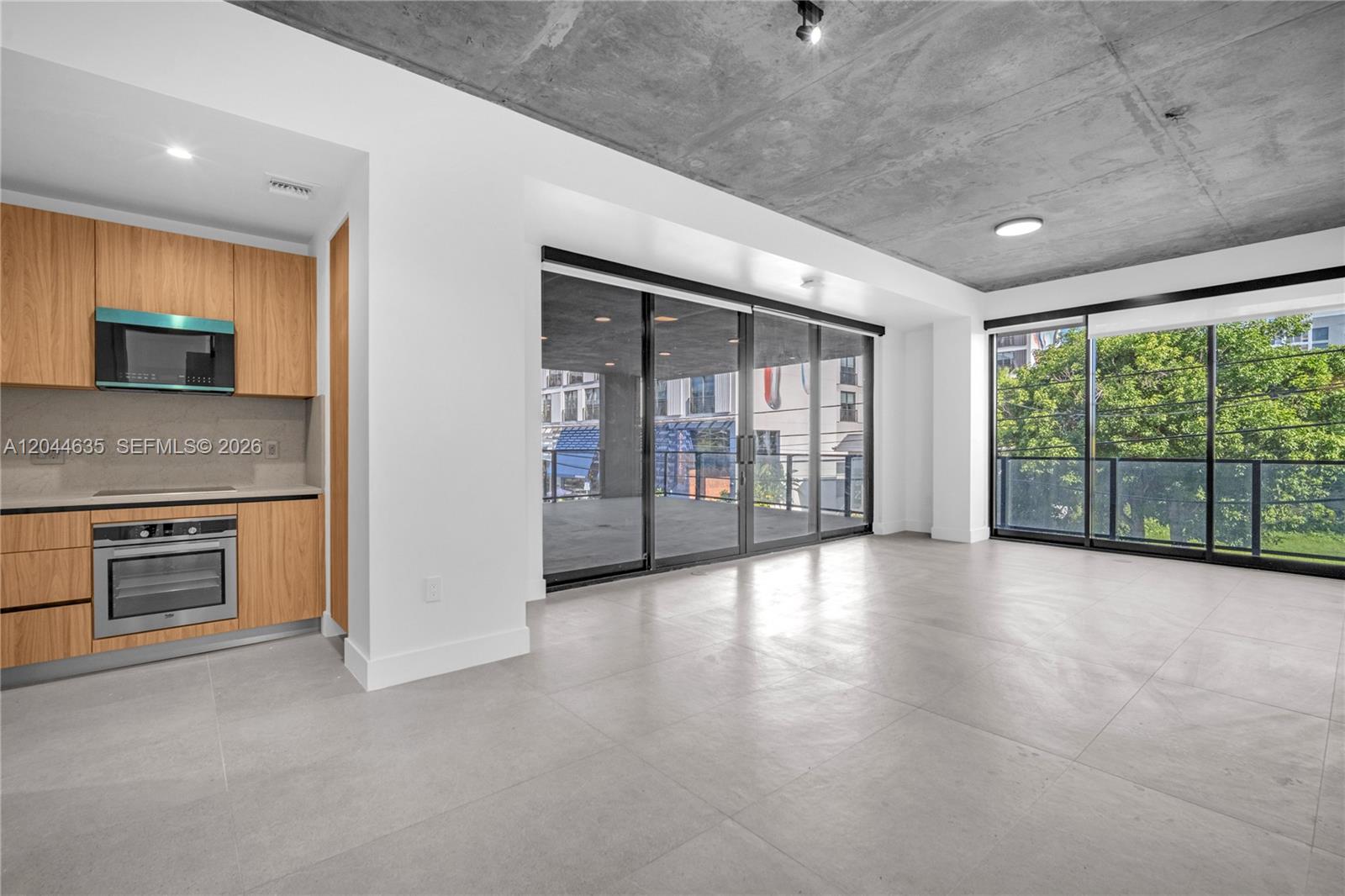 A modern kitchen and living area feature concrete ceilings, light tile floors, and glass doors — 91 NW 27th St # 101, Miami FL 33127, MIAMI, FL