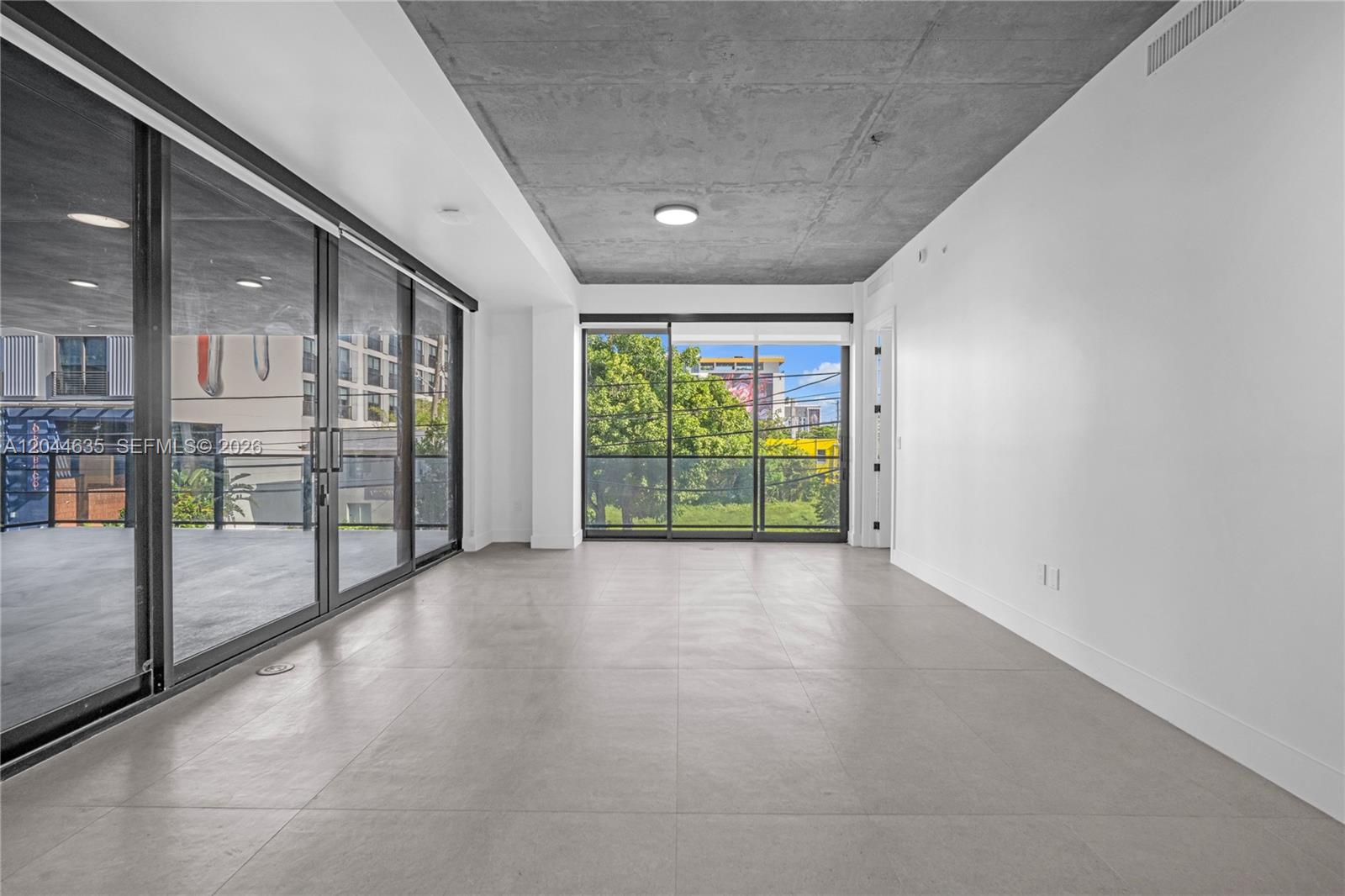 An empty room features a concrete ceiling, large sliding glass doors, and light-colored tile flooring — 91 NW 27th St # 101, Miami FL 33127, MIAMI, FL