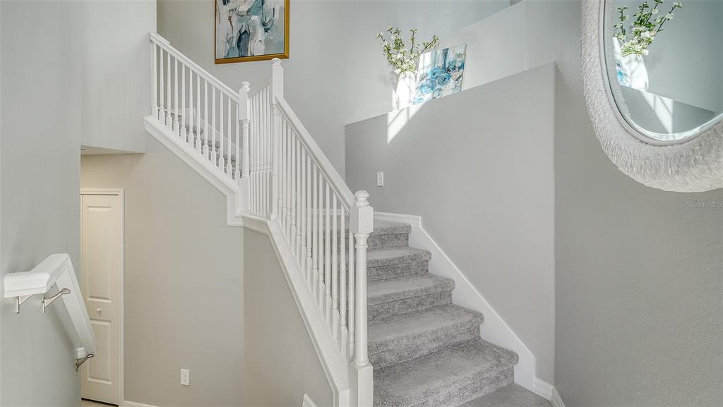 A staircase with gray carpet and white railings leads upward in a light-colored entryway — 17645 BOROCAY COURT UNIT 201, VENICE, FL