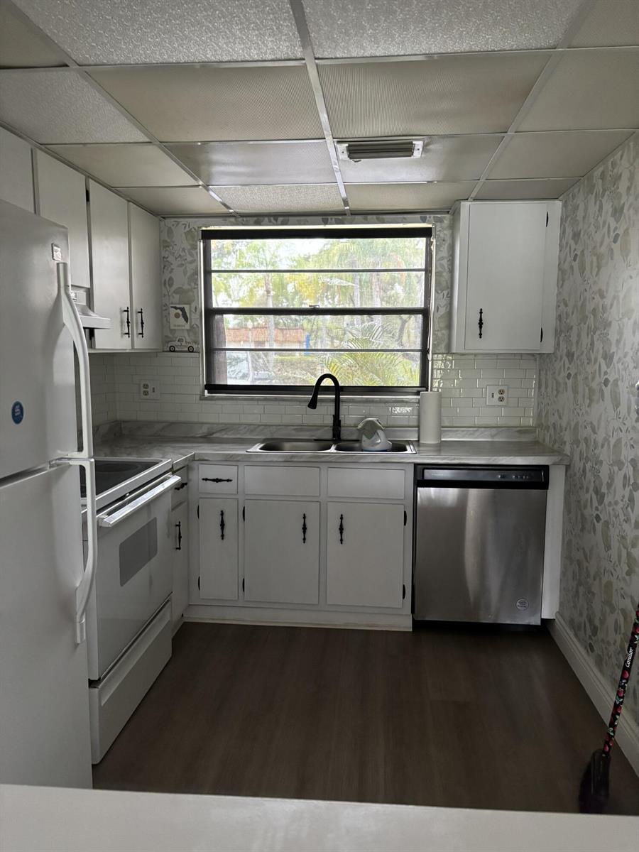 A kitchen features white cabinets, stainless steel appliances, a subway tile backsplash, and floral wallpaper — 2153 N 14th Avenue # 2153, Hollywood FL 33020, HOLLYWOOD, FL