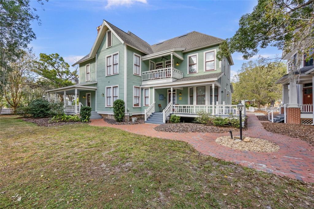 A two-story green house with a wrap-around porch and a brick walkway in the yard — 205 SE 7TH STREET, GAINESVILLE, FL