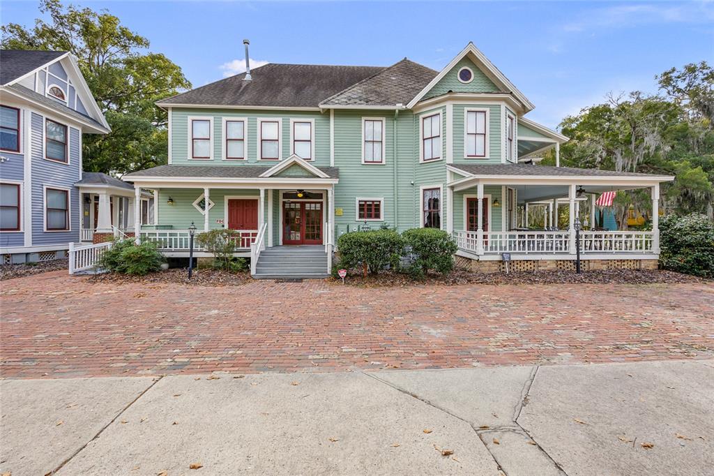 A two-story green house with a wrap-around porch and a brick driveway — 205 SE 7TH STREET, GAINESVILLE, FL