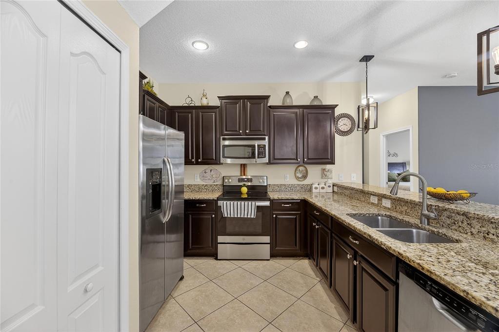 A kitchen features dark wood cabinets, granite countertops, stainless steel appliances, and tile flooring — 20041 SATIN LEAF AVENUE, TAMPA, FL