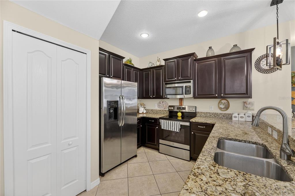 A kitchen features dark wood cabinets, granite countertops, stainless steel appliances, and tile flooring — 20041 SATIN LEAF AVENUE, TAMPA, FL