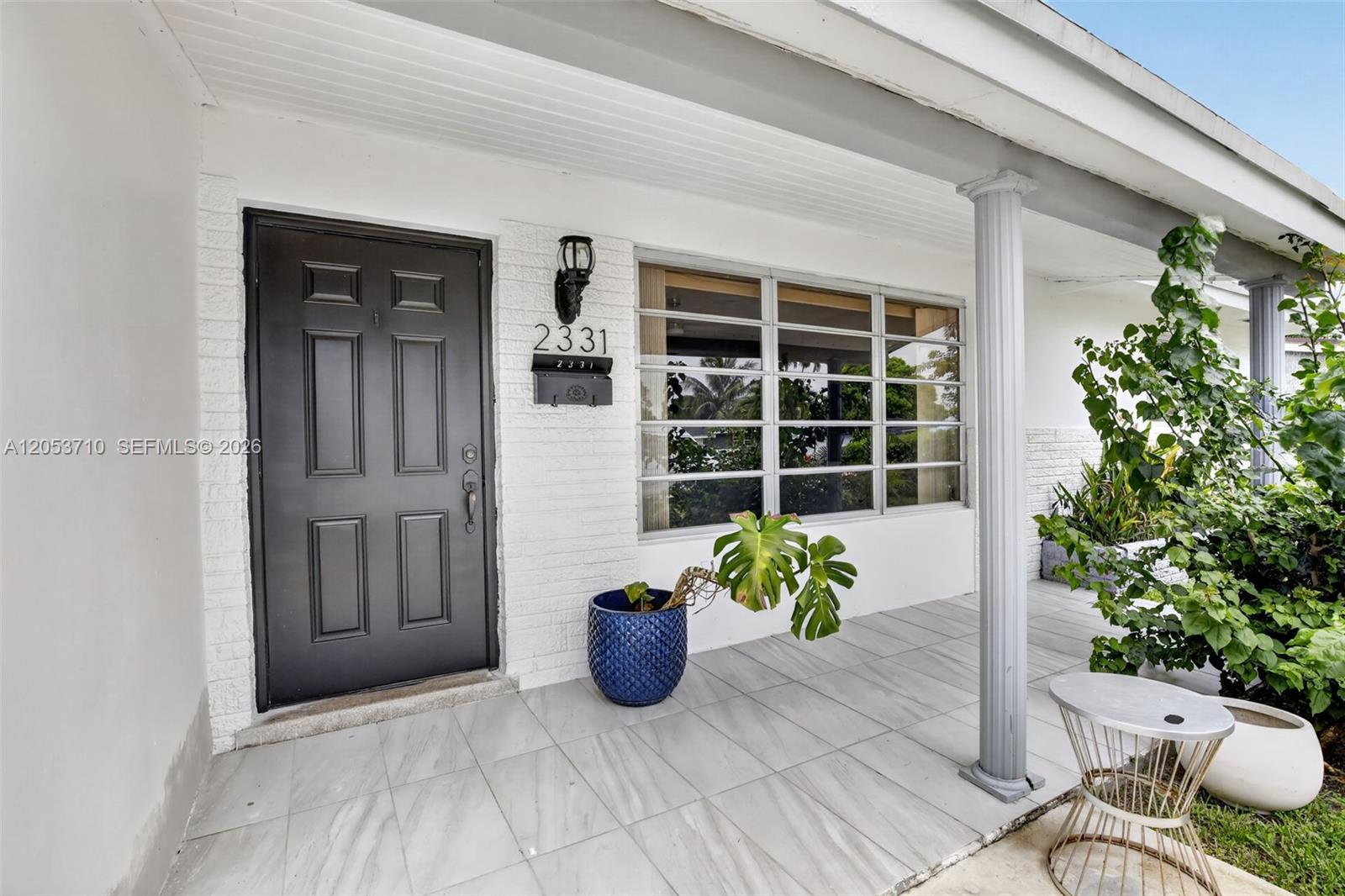 A covered porch features white brick walls, a dark front door, and tiled flooring — 2331 Flamingo Dr, Miramar FL 33023, MIRAMAR, FL