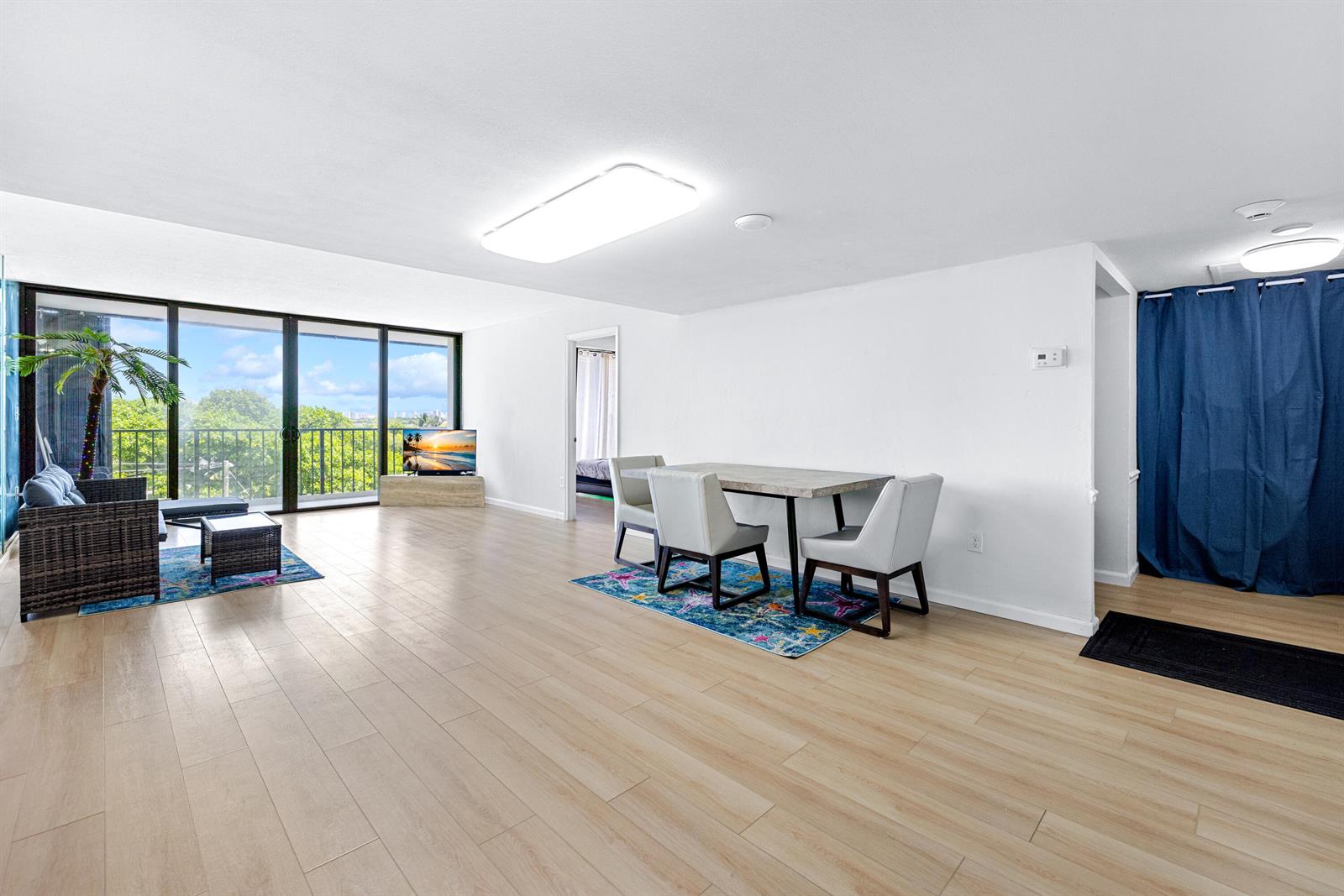 A living and dining area with light wood flooring, large sliding glass doors, and furniture — 5600 N Flagler Drive # 407, West Palm Beach FL 33407, WEST PALM BEACH, FL