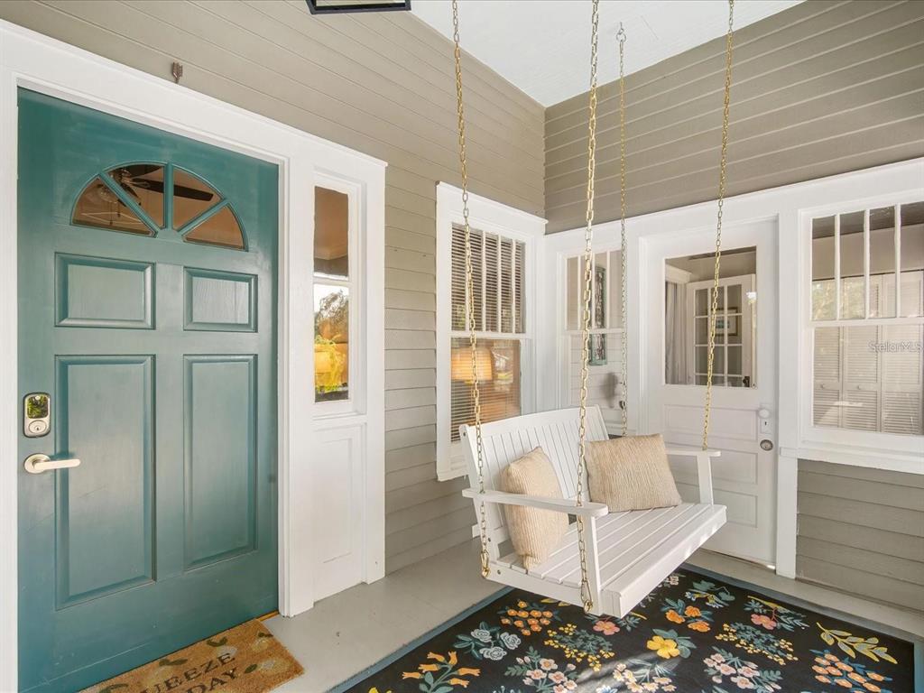 A porch features a teal front door, a white hanging swing, and a floral rug — 2822 4TH AVENUE W, BRADENTON, FL