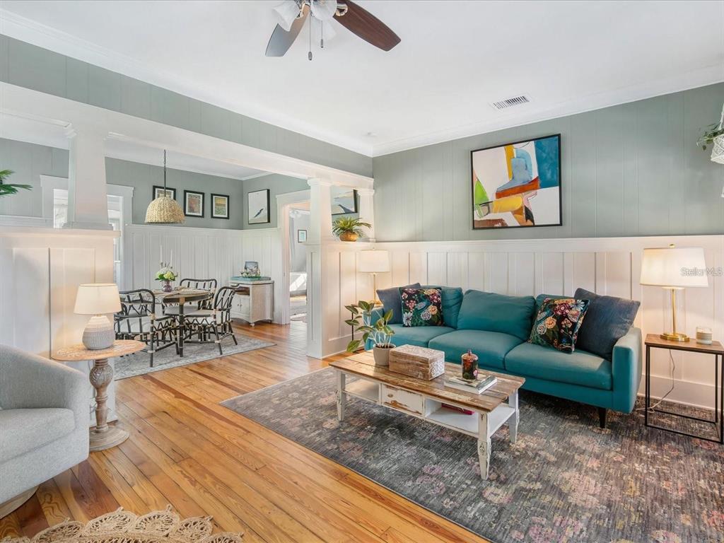 A living room with a teal sofa, wood floors, and a dining area in the background — 2822 4TH AVENUE W, BRADENTON, FL