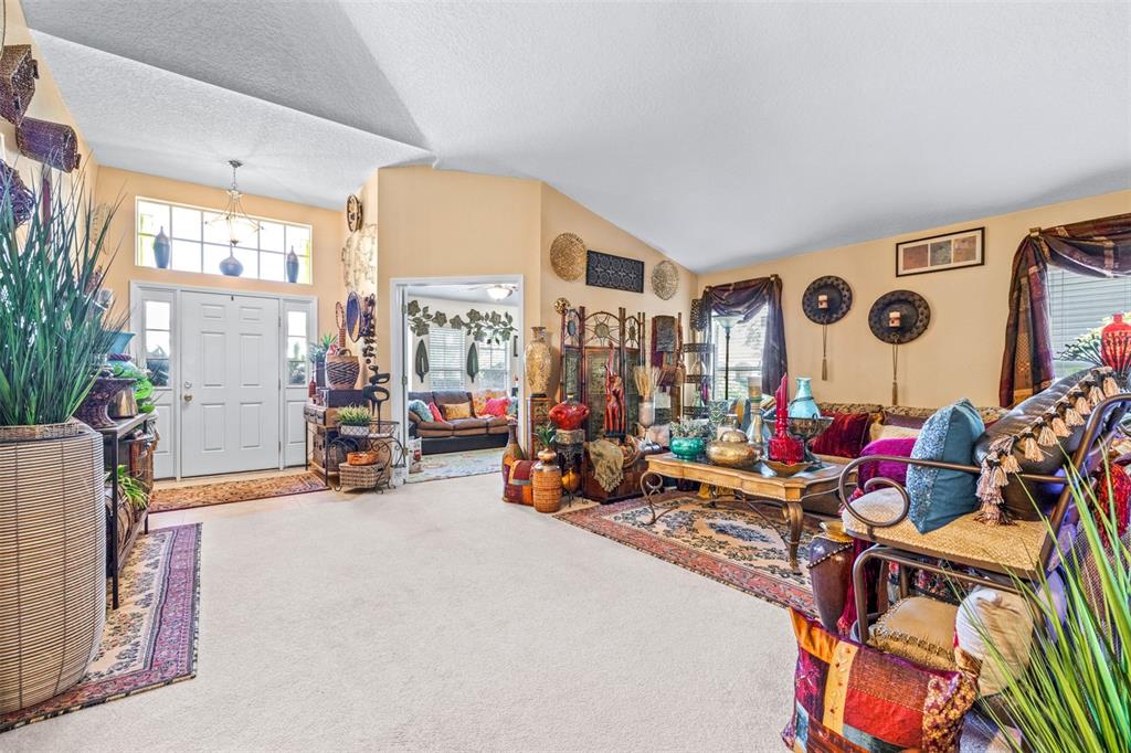 A spacious living room features vaulted ceilings, beige walls, carpeted floors, and eclectic decor — 7113 CROMWELL PARK LANE, APOLLO BEACH, FL